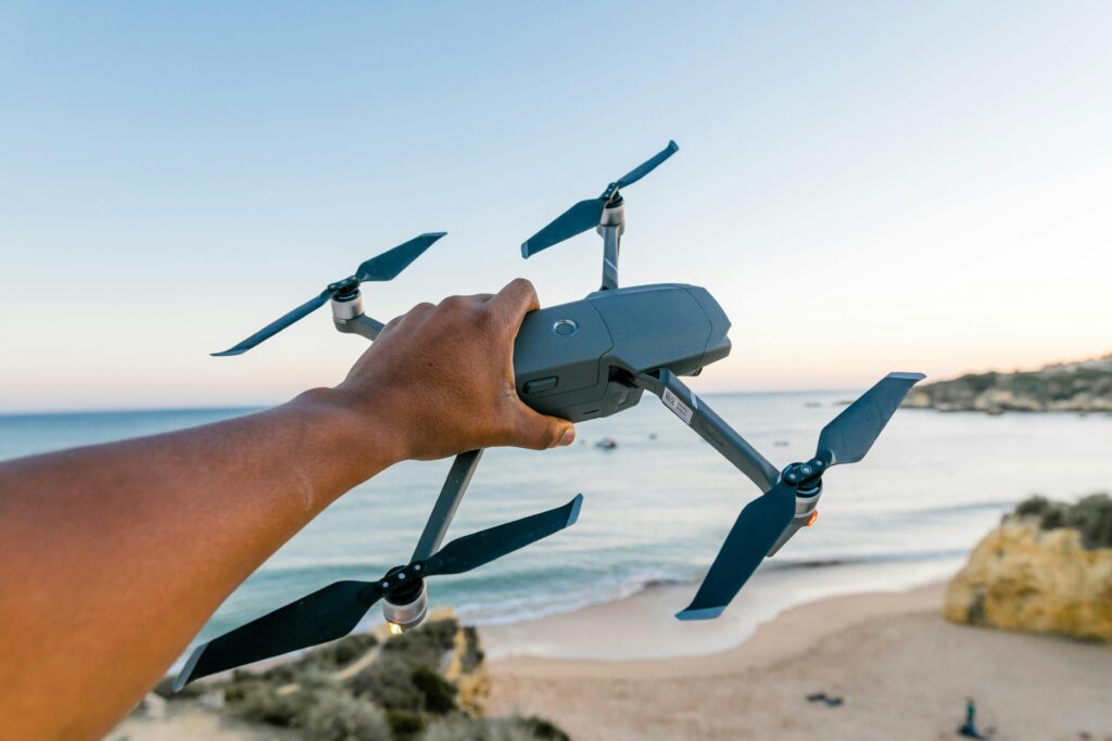 A hand holding a drone over a beach in Albufeira, Portugal, during sunset, showcasing technology and travel. lazygenie